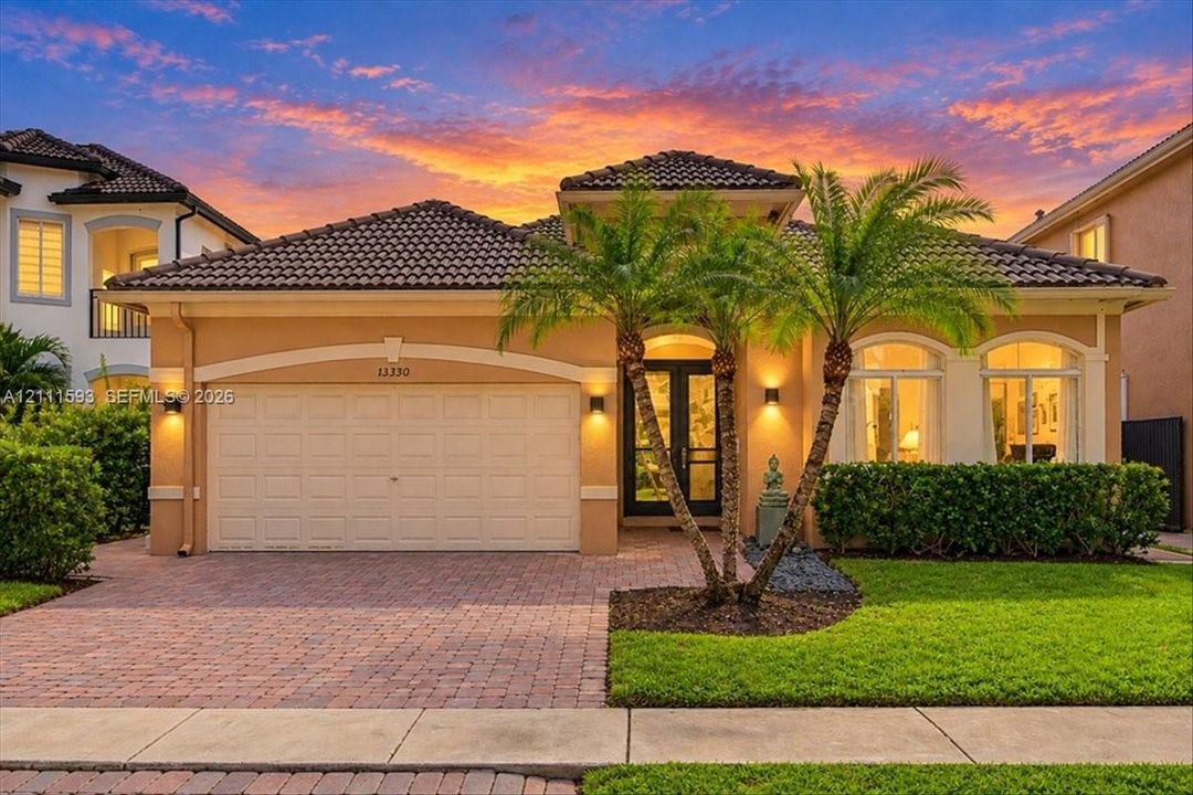Stucco exterior featuring a tile roof, arched entryway, brick-paver driveway, and manicured landscaping