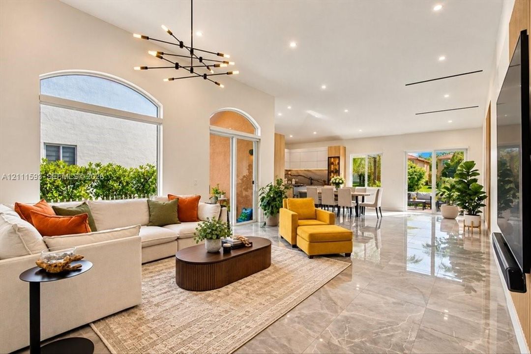 Open-concept living space featuring high ceilings, polished stone-finish flooring, a large arched window, recessed lighting, and a multi-arm geometric chandelier