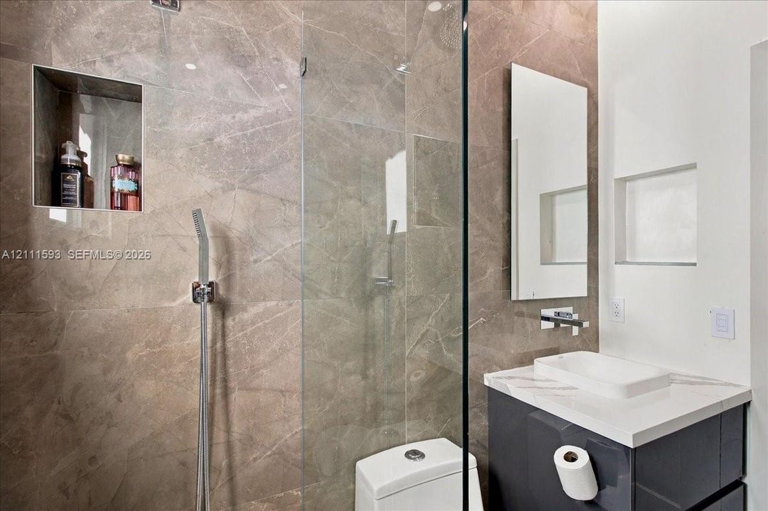 Walk-in shower with floor-to-ceiling large-format tile, glass enclosure, and built-in recessed wall niche, featuring a modern wall-mounted vanity with a rectangular vessel sink and wall-mounted faucet