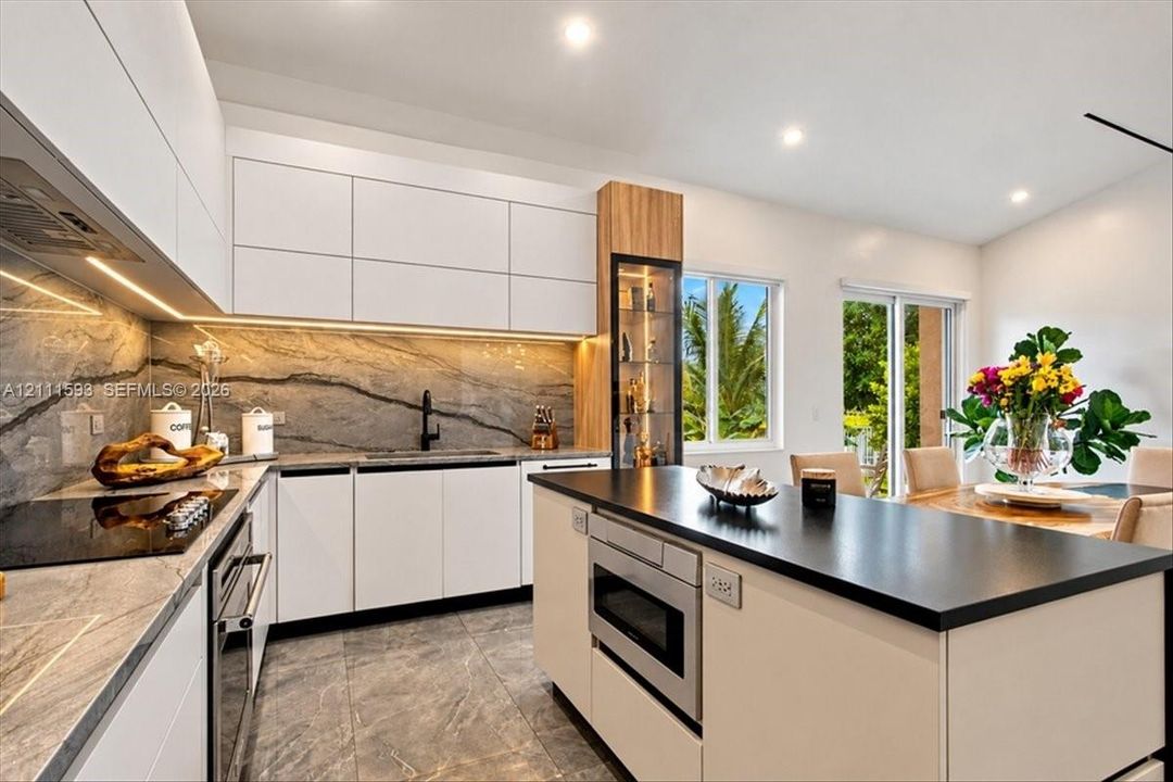 Kitchen featuring white flat-panel cabinetry, stone-patterned backsplash, built-in display shelving, center island with a dark countertop, and recessed lighting