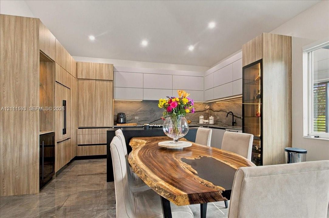 Modern kitchen featuring dual-tone cabinetry, integrated appliances, stone-surface backsplash, wood-finish paneling, and polished stone flooring