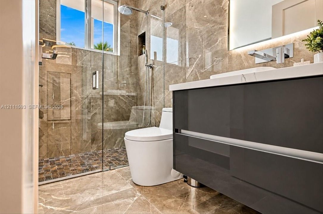 Bathroom featuring a floating vanity with a vessel sink, wall-mounted faucet, walk-in shower with a glass enclosure, and large-format tile flooring with a pebble-style shower floor