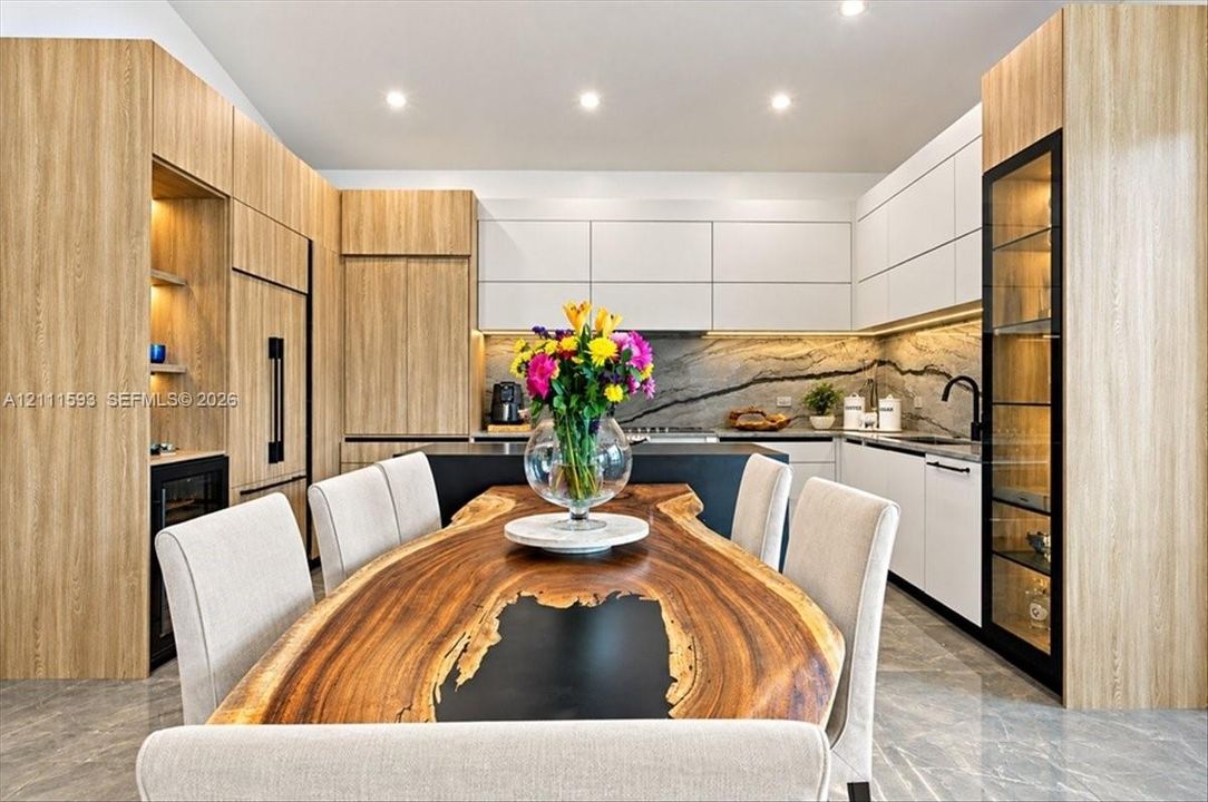 Modern kitchen featuring flat-panel wood-finish cabinetry, white slab-style upper cabinets, veined stone-finish backsplash, integrated wine refrigerator, and a floor-to-ceiling glass display cabinet