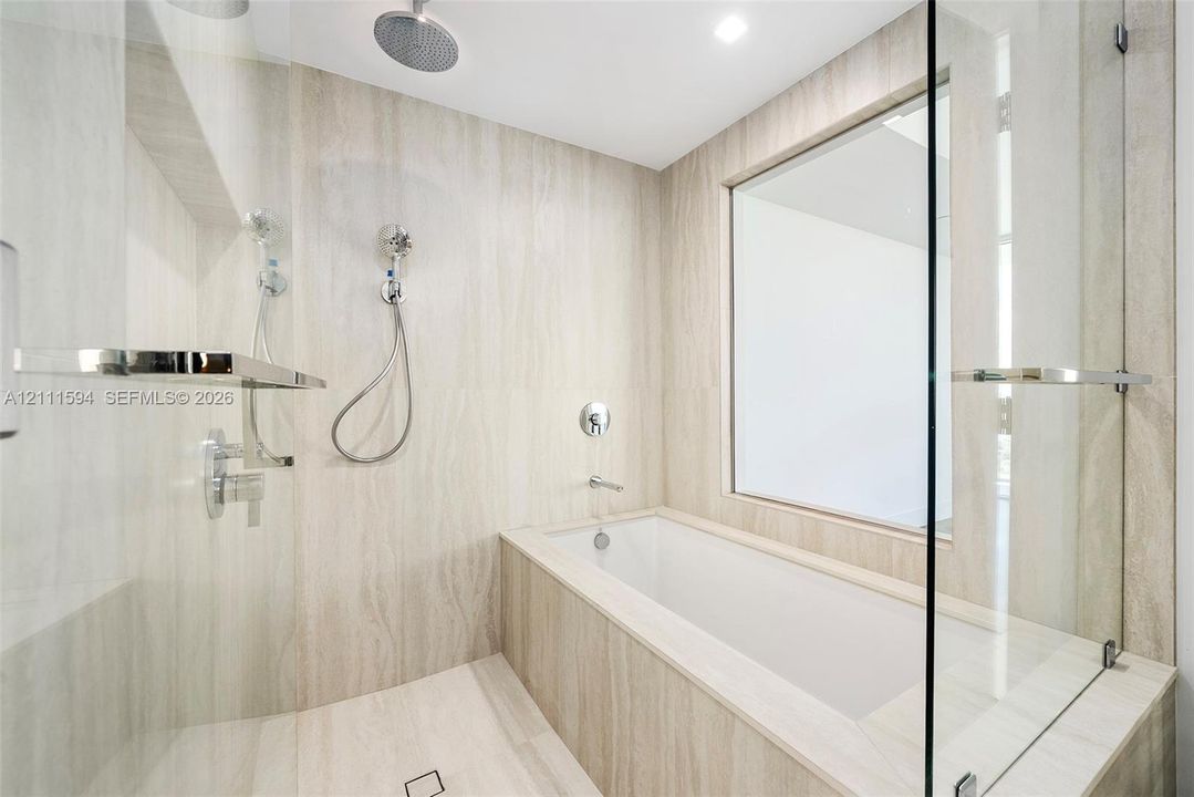 Wet room featuring stone-finish wall and floor tiling, deep-soaking bathtub, glass partition, wall-mounted shower system with rain head, and integrated shelving