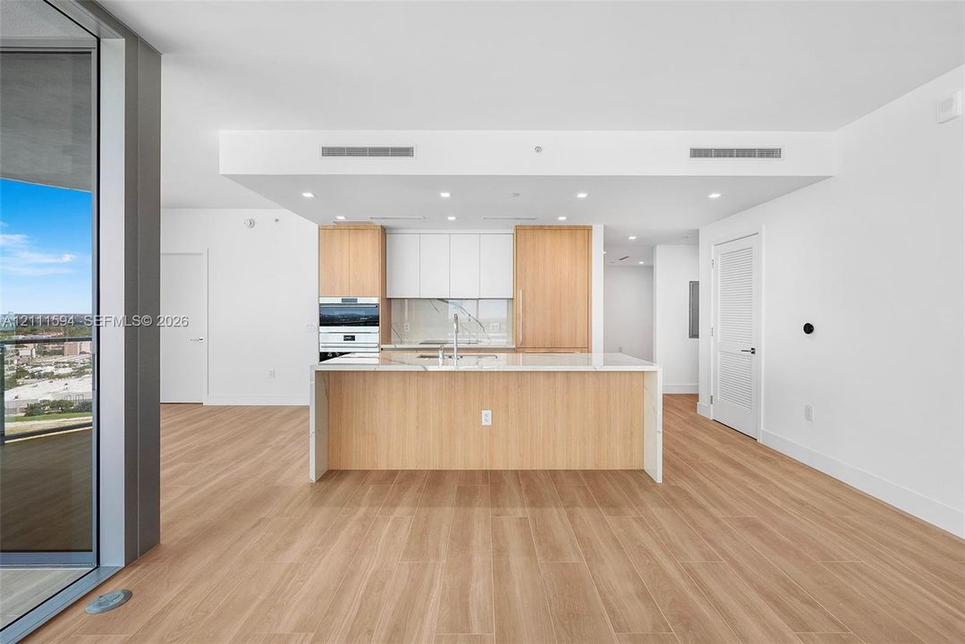 Kitchen featuring wood-finish cabinetry, white slab countertops, a central island, recessed lighting, and integrated wall oven
