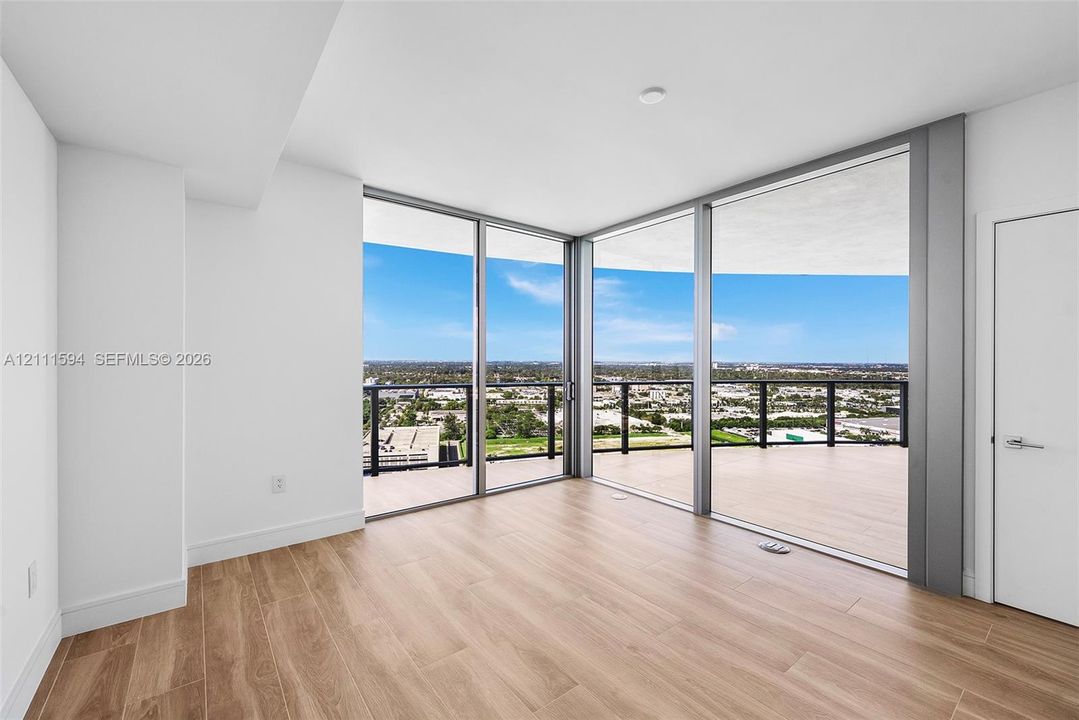 Floor-to-ceiling glass corner walls, wood-finish flooring, and expansive wrap-around balcony with metal railings