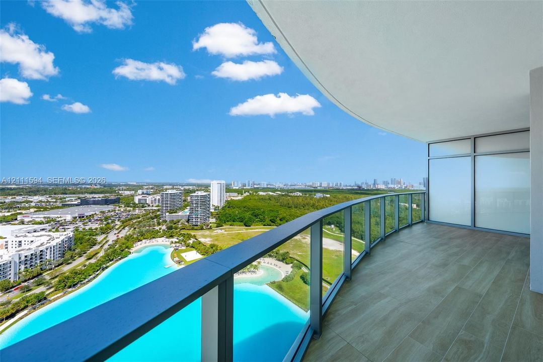 Curved balcony featuring wood-finish tile flooring, glass railings, and expansive architectural overhang