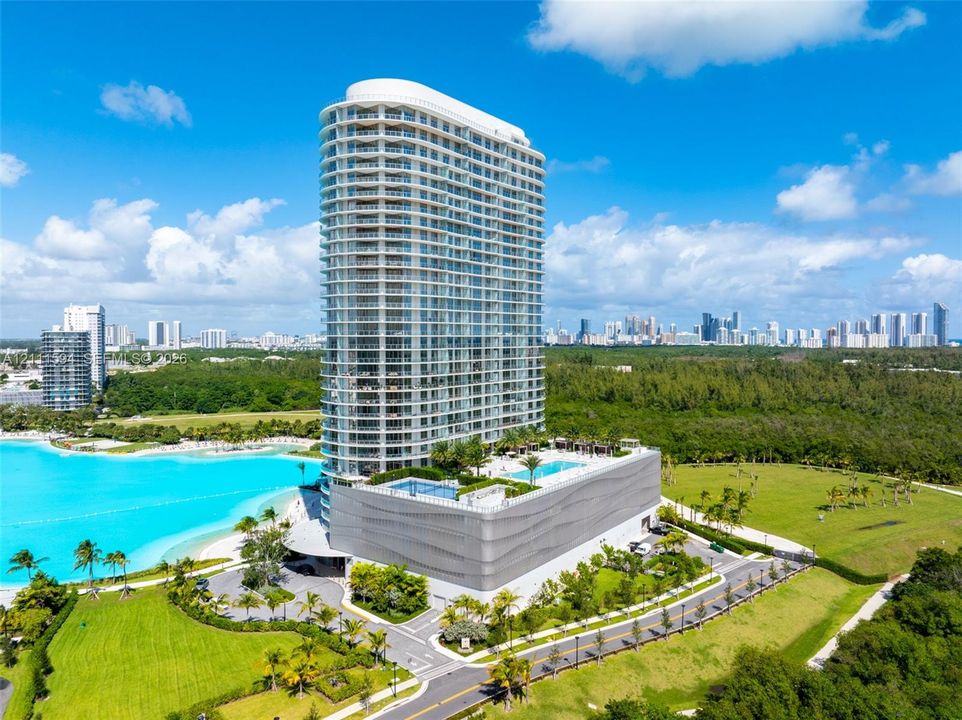 High-rise building featuring a glass facade, multiple wraparound balconies, an elevated swimming pool, and curated landscape grounds