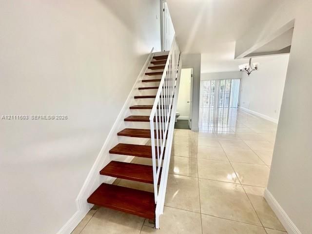Staircase featuring wood-finish treads and white metal railings, complemented by large-format tile flooring and an overhead chandelier