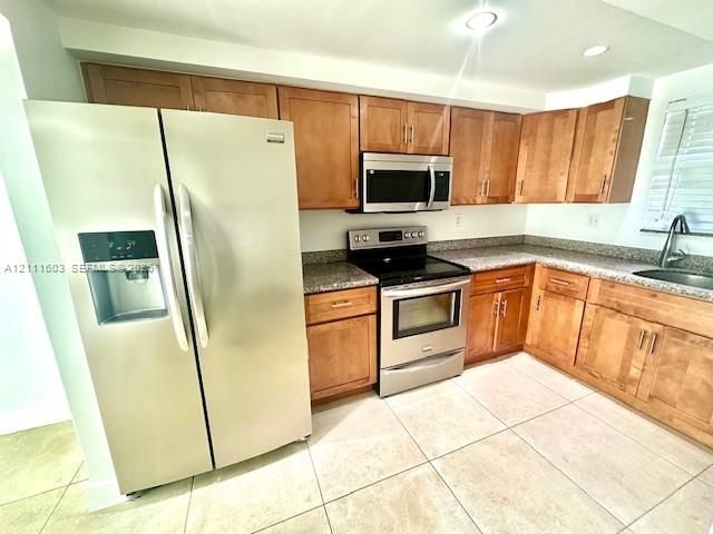 Kitchen featuring wood cabinetry, stainless steel appliances, speckled stone-finish countertops, and ceramic tile flooring