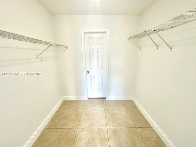 Storage space featuring wall-mounted wire shelving, neutral ceramic tile flooring, and a six-panel door