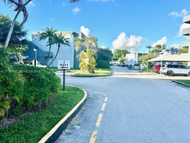 Exterior view featuring paved driveways, covered parking structures, mature palm trees, and manicured landscaping