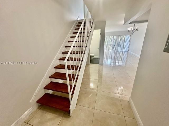 Staircase featuring wood-finish treads and white metal railings, complemented by large-format tile flooring