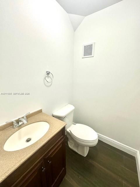 Bathroom featuring a wood-finish vanity with a molded countertop and oval integrated basin, chrome double-handle faucet, elongated toilet, and wood-finish flooring