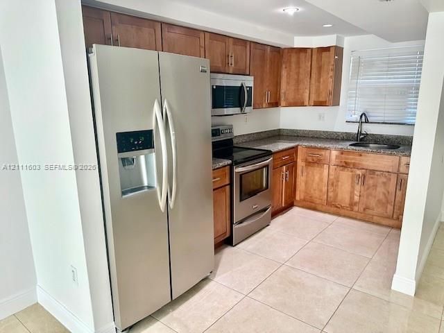 Kitchen featuring medium-toned wood cabinetry, stainless steel appliances, stone-surface countertops, and tile flooring