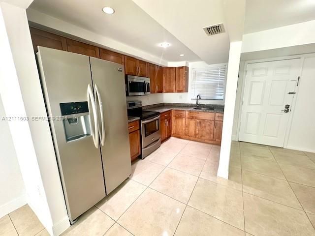 Kitchen featuring wood cabinetry, stainless steel appliances, stone-surface countertops, recessed lighting, and large-format tile flooring