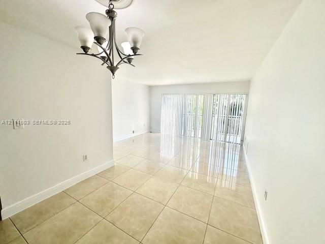 Neutral ceramic tile flooring, five-light iron chandelier, and floor-to-ceiling sliding glass doors with vertical blinds