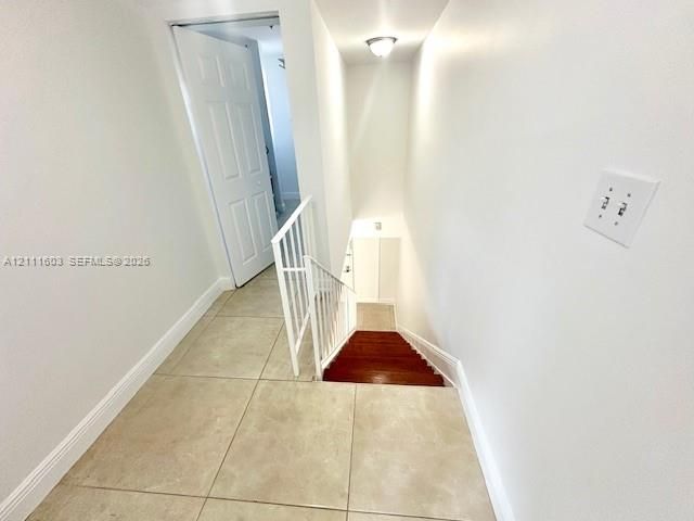Large-format tile flooring, white six-panel interior door, wood-finish staircase, and white metal handrailing