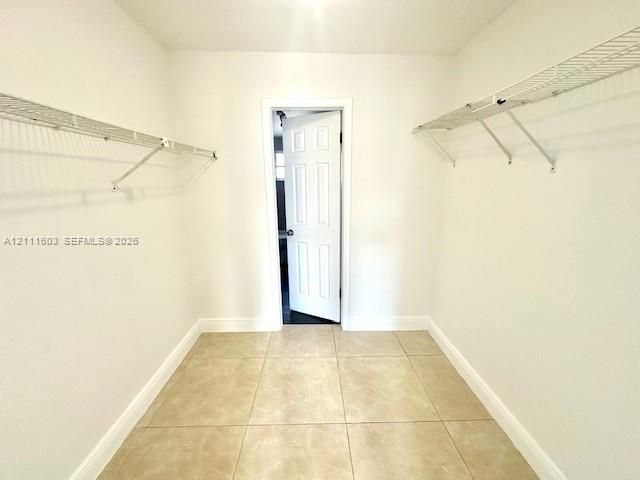 Walk-in storage area featuring neutral tile flooring, white walls, and dual-level wire shelving