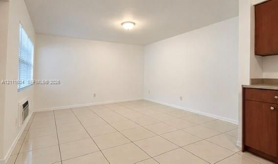 Neutral-toned tile flooring, flush-mount ceiling lighting, and large-format window with horizontal blinds