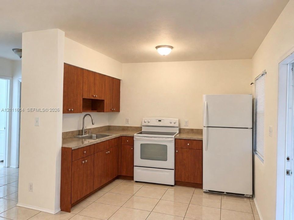 Kitchen featuring wood-finish cabinetry, neutral solid-surface countertops, tile flooring, and white kitchen appliances