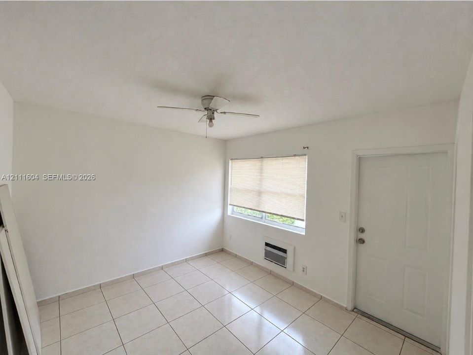 Room featuring neutral wall-to-wall ceramic tile flooring, a ceiling fan, and a wall-mounted climate control unit