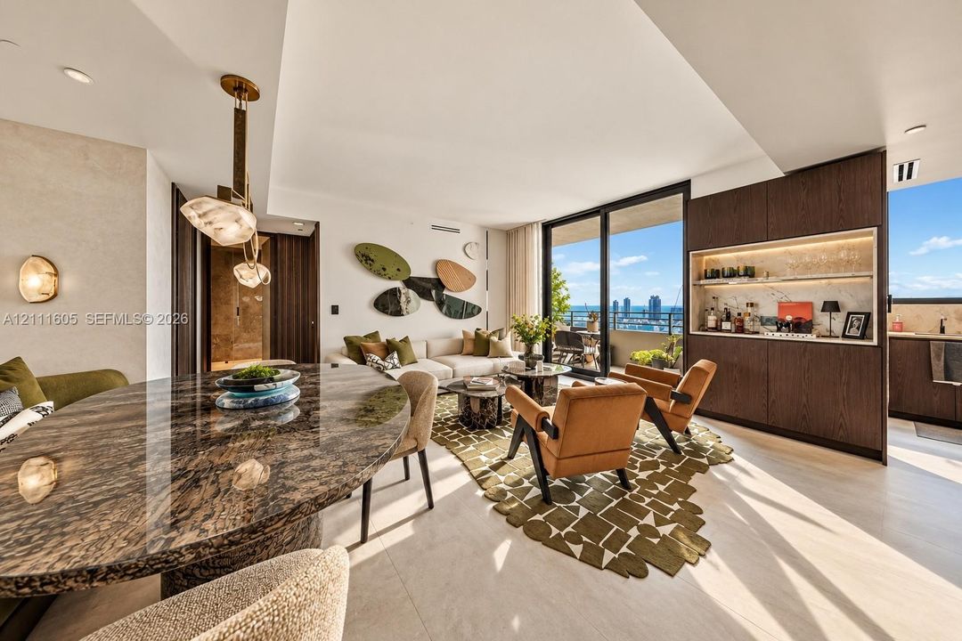 Open-concept living space featuring high-gloss stone-surface dining table, floor-to-ceiling glass sliding doors, built-in dark wood cabinetry with integrated shelving, metallic pendant lighting, and neutral large-format tile flooring