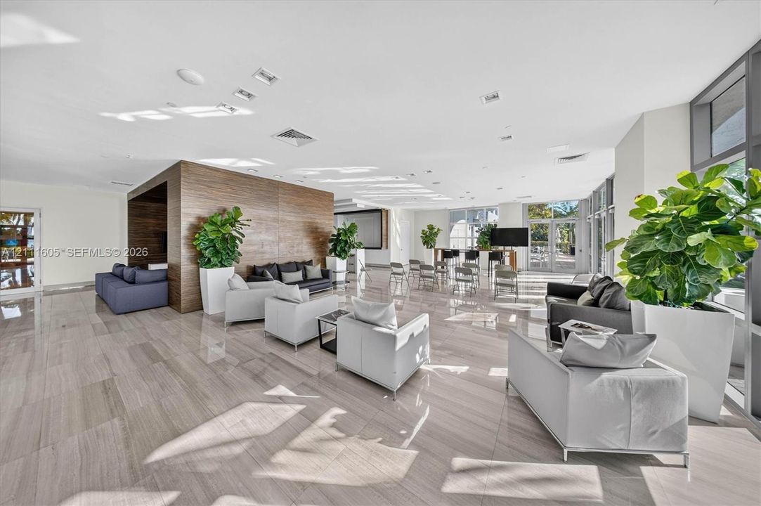 Open-concept common area featuring large-format stone-finish flooring, wood-paneled accent wall, and expansive floor-to-ceiling windows