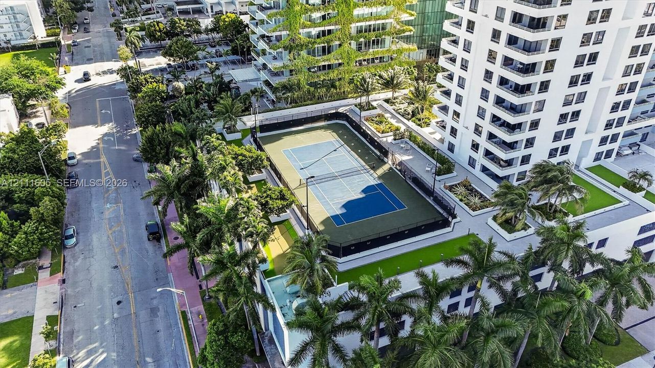 Hard-surface tennis court featuring perimeter fencing, surrounded by landscaped greenery, mature palm trees, and manicured lawns