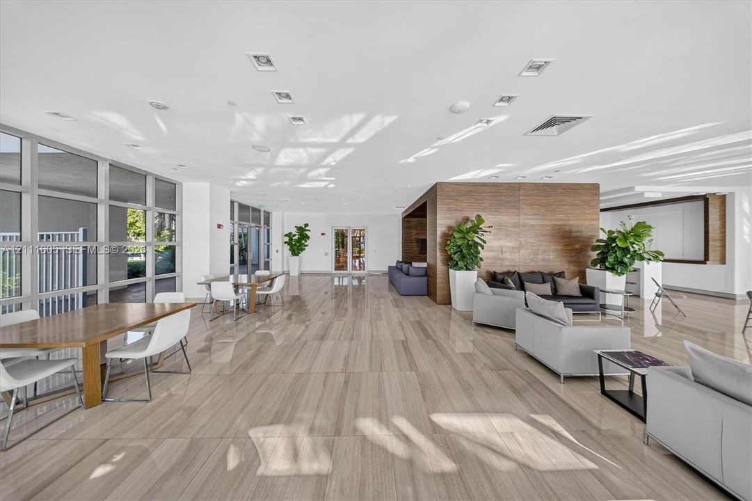 Spacious communal area featuring large-format stone-finish flooring, full-height glass window panels, and a prominent wood-panel accent wall with integrated recessed lighting