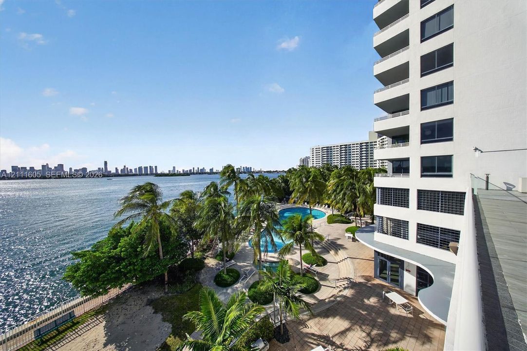 High-rise residential exterior with multi-level private balconies, waterfront swimming pool, manicured grounds featuring mature palm trees, and hardscaped patio areas