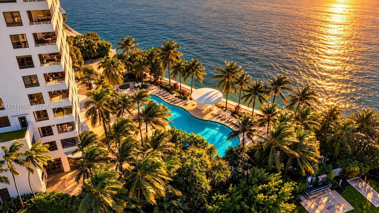 High-rise exterior featuring private balconies, a multi-level swimming pool, extensive palm tree landscaping, and direct access to the oceanfront