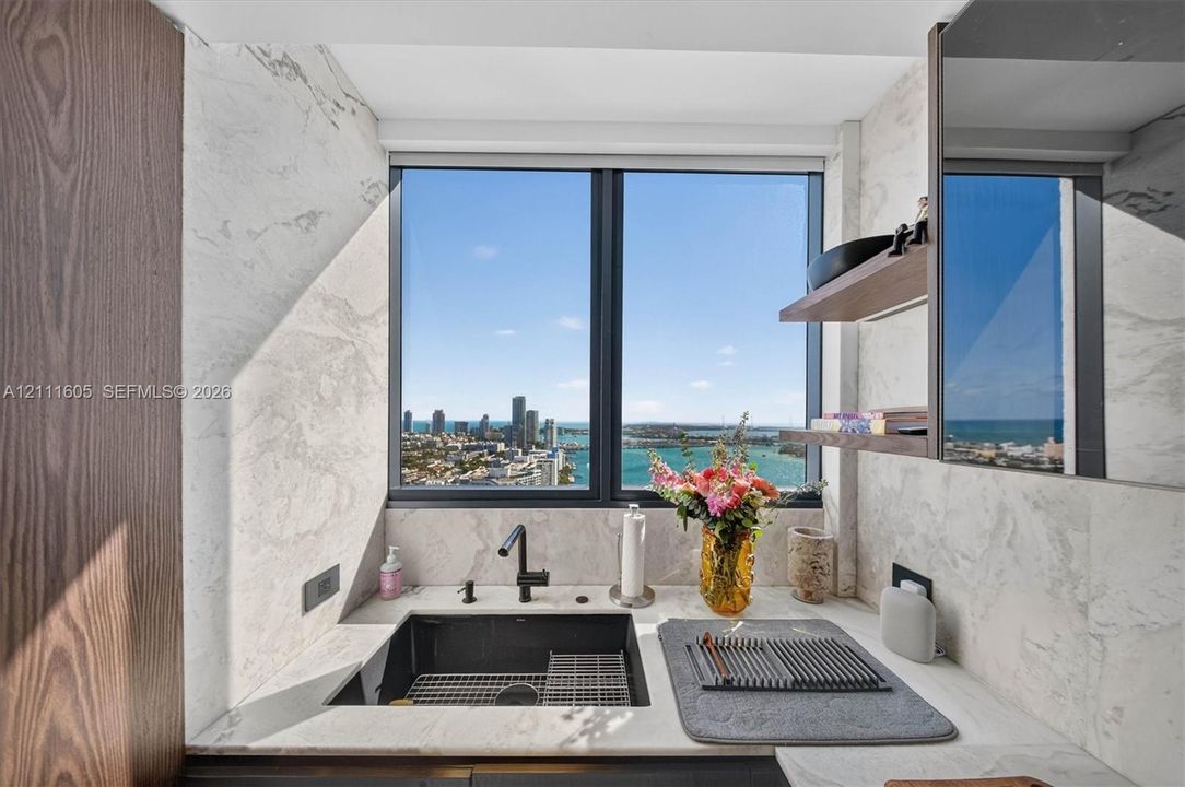Stone countertop, undermount sink, matte black hardware, stone-finish wall cladding, and wood-finish cabinetry