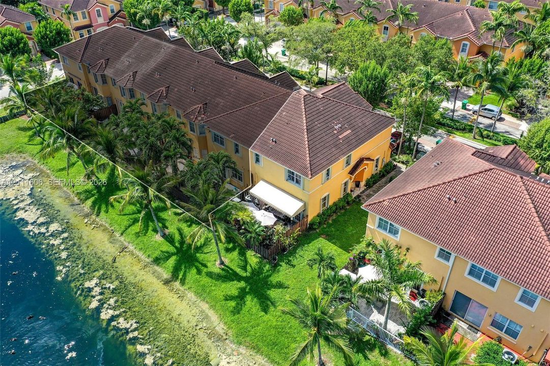 Waterfront residence featuring a tile roof, stucco exterior, rear patio, and established tropical landscaping