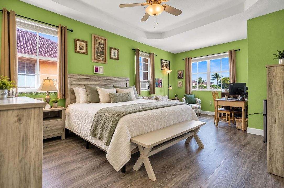 Tray ceiling featuring a central lighted ceiling fan, wood-finish flooring, and multiple large windows