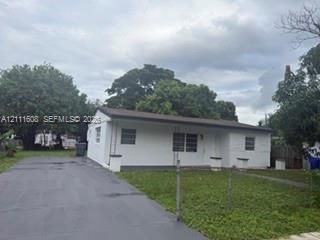Single-story exterior featuring a white masonry facade, horizontal roofline, long concrete driveway, and front lawn