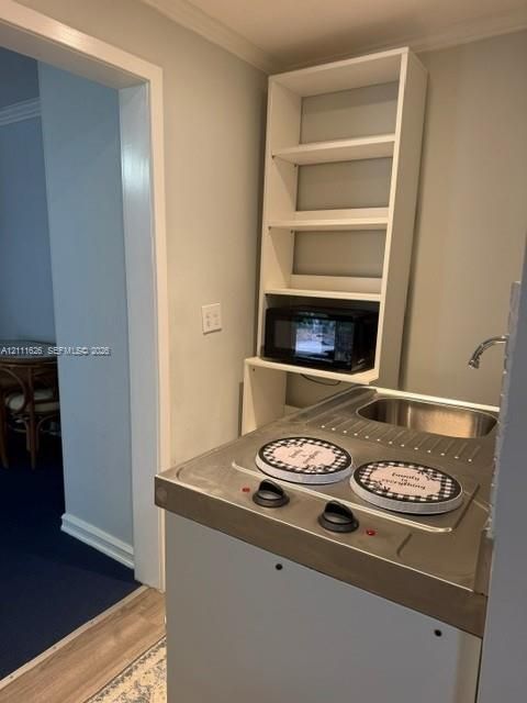 Compact kitchenette station featuring a stainless steel drop-in sink, dual-burner cooktop, and built-in floor-to-ceiling white shelving