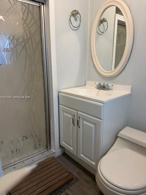 Bathroom featuring a white vanity cabinet with an integrated sink, shower enclosure with patterned glass, oval wall-mounted mirror, and wood-finish flooring
