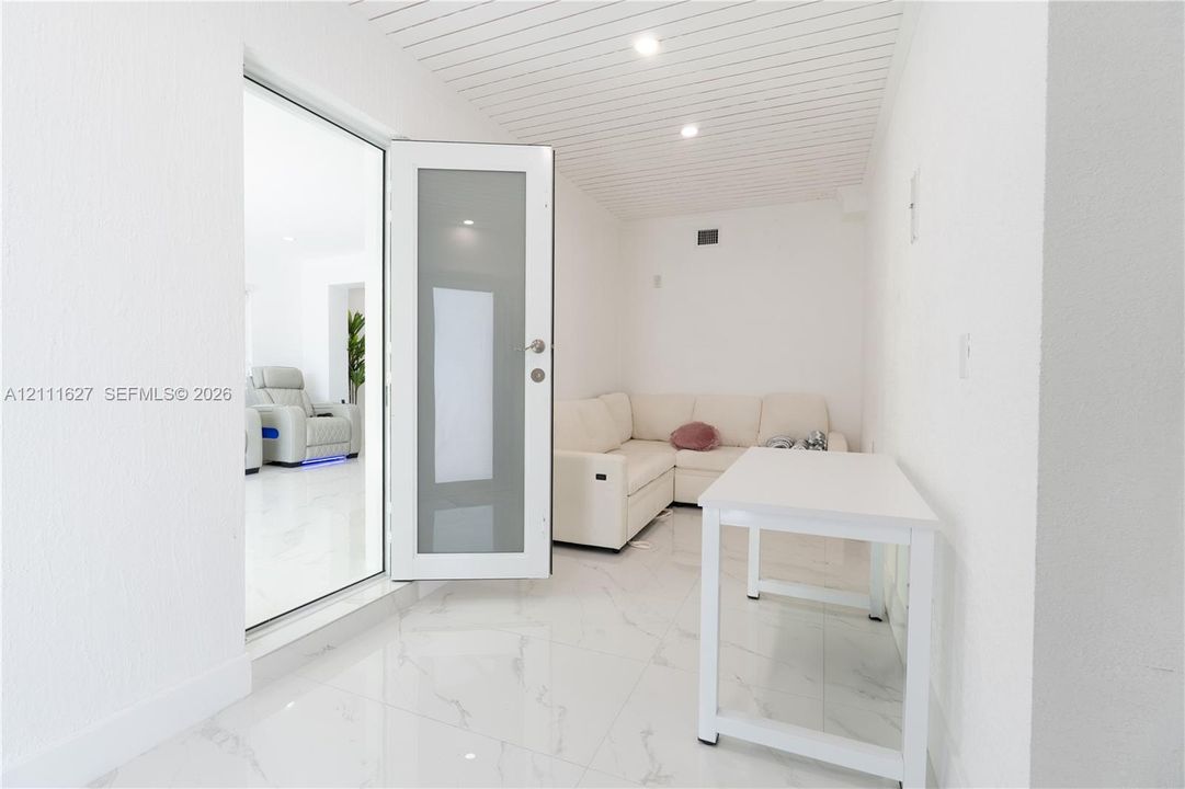 Interior space featuring polished white tile flooring, a frosted glass-panel door, and a white beadboard ceiling with recessed lighting