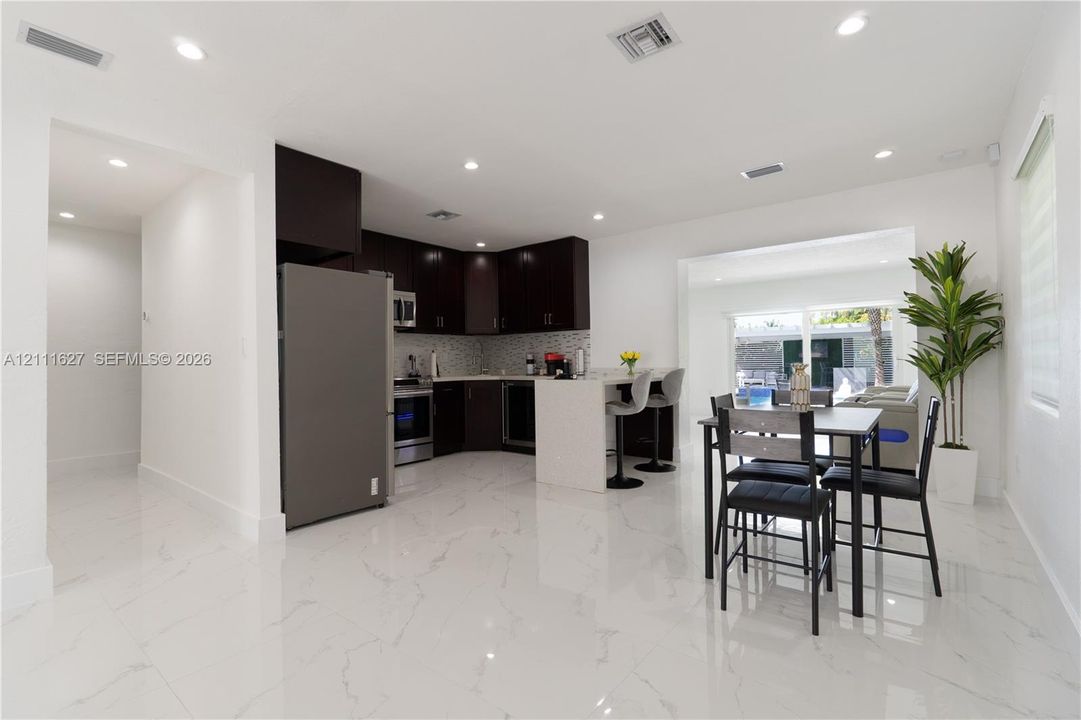 Kitchen featuring dark-toned cabinetry, a stone-finish countertop island with a breakfast bar, stainless steel appliances, a mosaic-tile backsplash, and polished stone-finish flooring
