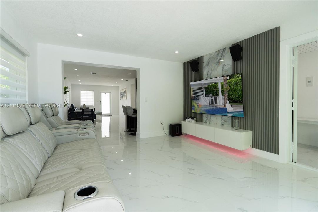 Living area featuring polished tile flooring, a wall-mounted floating media cabinet, and a decorative accent wall with vertical slat paneling and stone-finish cladding