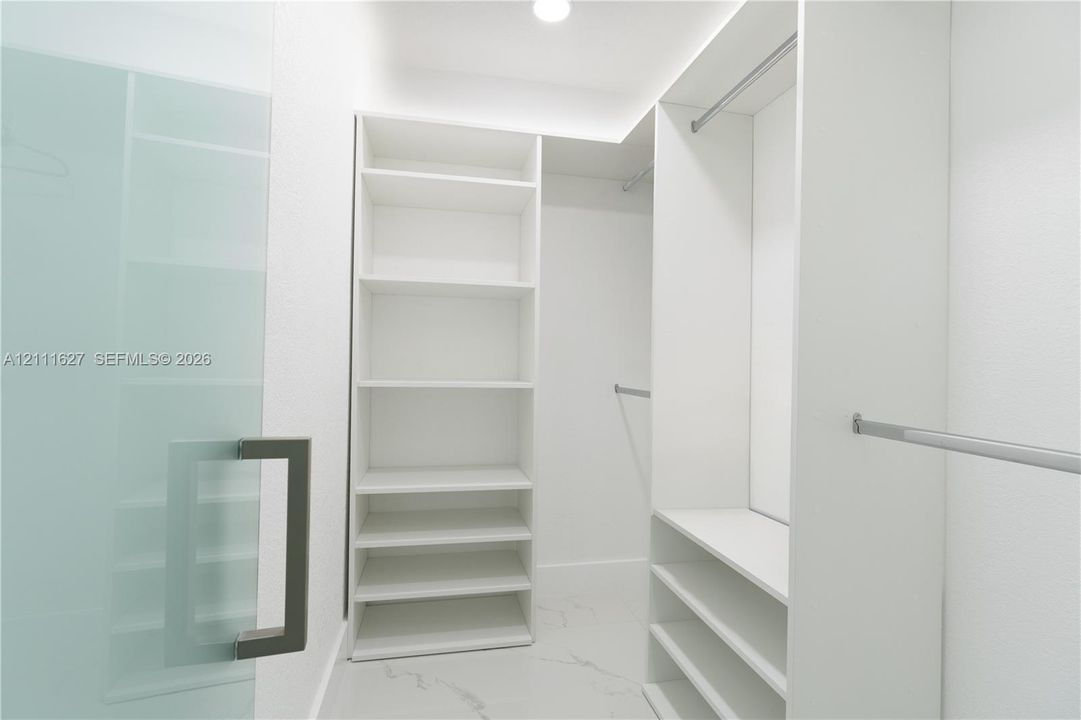 Custom walk-in closet featuring white built-in shelving, floor-to-ceiling storage units, multiple metal hanging rods, and stone-finish tile flooring
