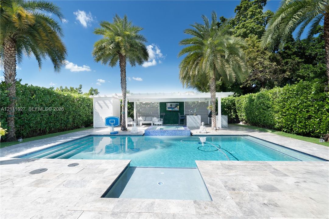 Swimming pool with built-in spa, stone paver patio, covered cabana, and perimeter privacy hedges