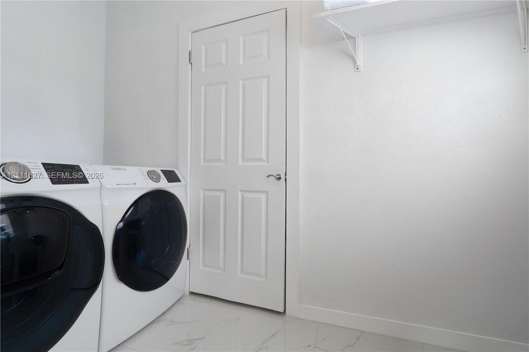 Laundry room featuring large-format tile flooring, a six-panel door with brushed nickel hardware, and an overhead built-in white storage shelf