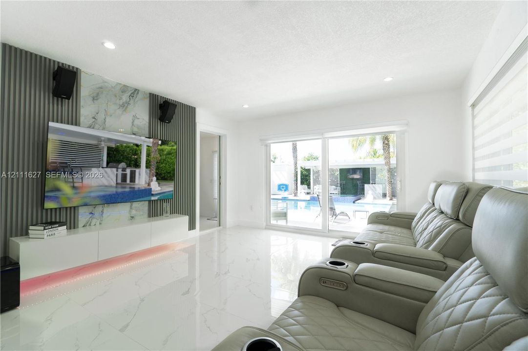 Polished stone-finish flooring, custom accent wall featuring vertical slats and a natural stone-finish inset, integrated low-profile cabinetry with under-cabinet lighting, and expansive sliding glass doors