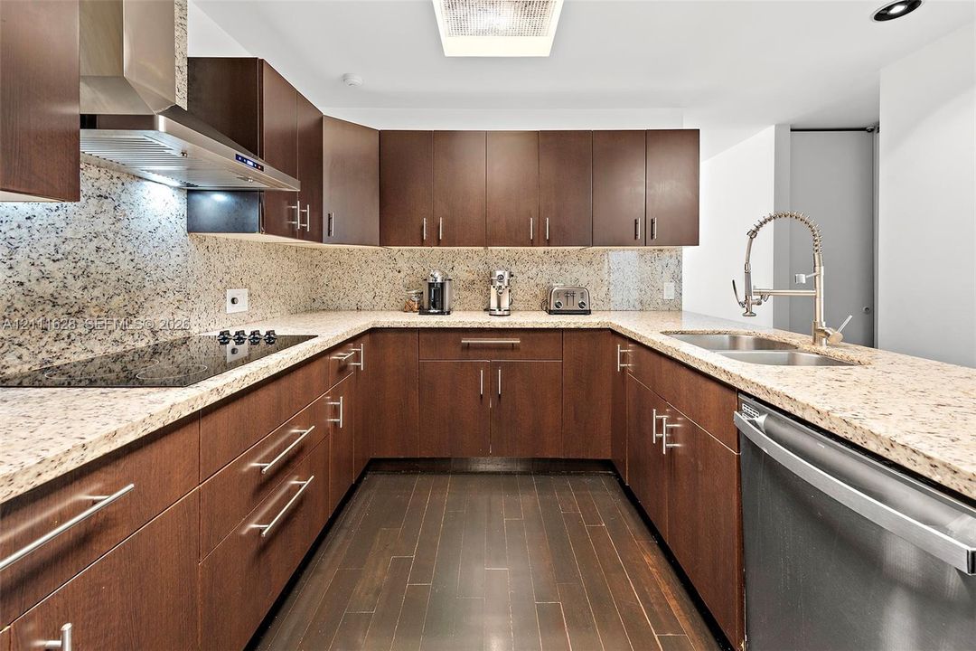 Kitchen featuring dark wood-finish cabinetry, stone countertops, stone backsplash, stainless steel appliances, and wood-finish flooring