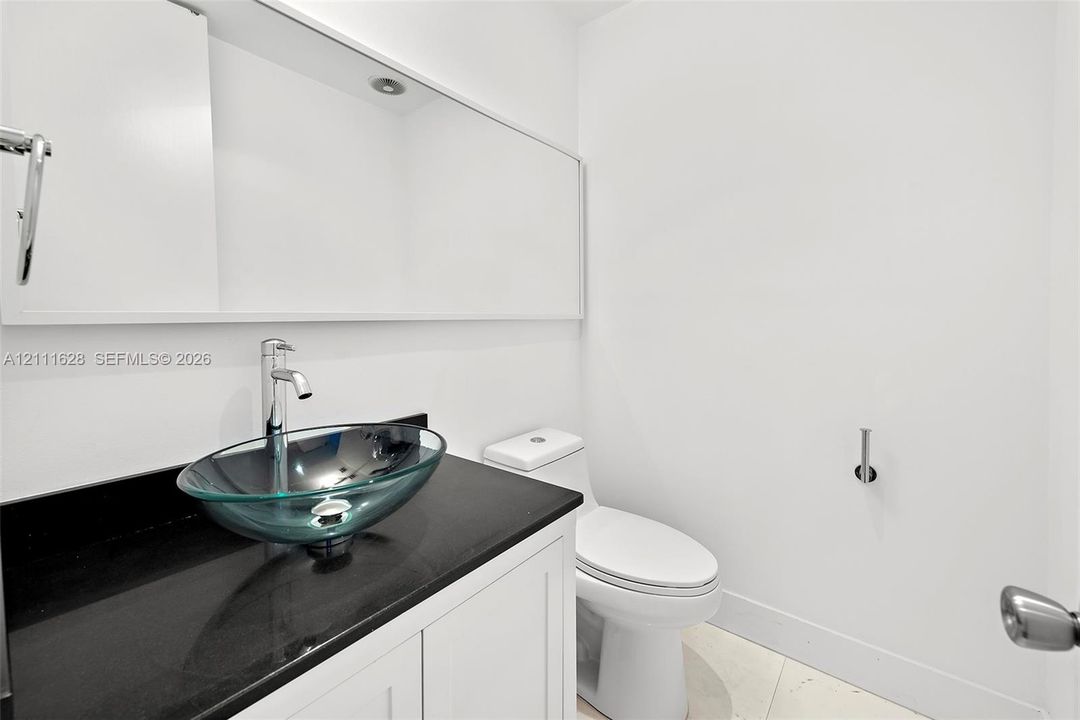 Built-in vanity featuring a dark stone countertop, clear glass vessel sink, chrome faucet, and expansive wall-mounted mirror