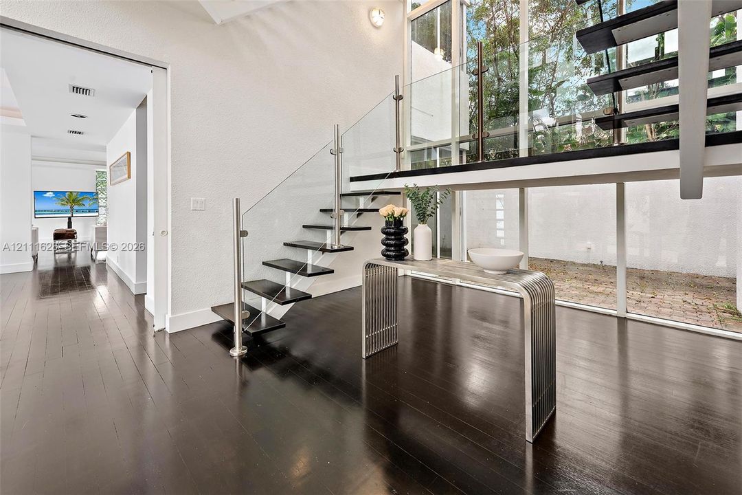 Floating staircase with dark wood-finish treads, glass railing, stainless steel hardware, floor-to-ceiling windows, and dark wood-finish flooring