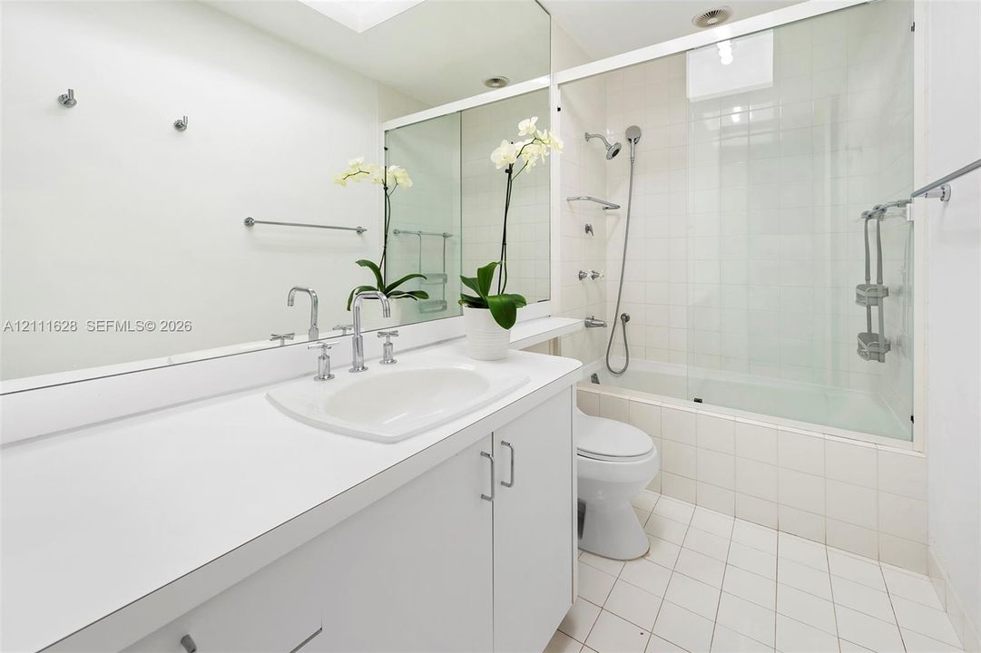 Bathroom featuring a white vanity with an integrated sink, polished chrome fixtures, a large wall-mounted mirror, and a tub-shower combination enclosed by a glass panel