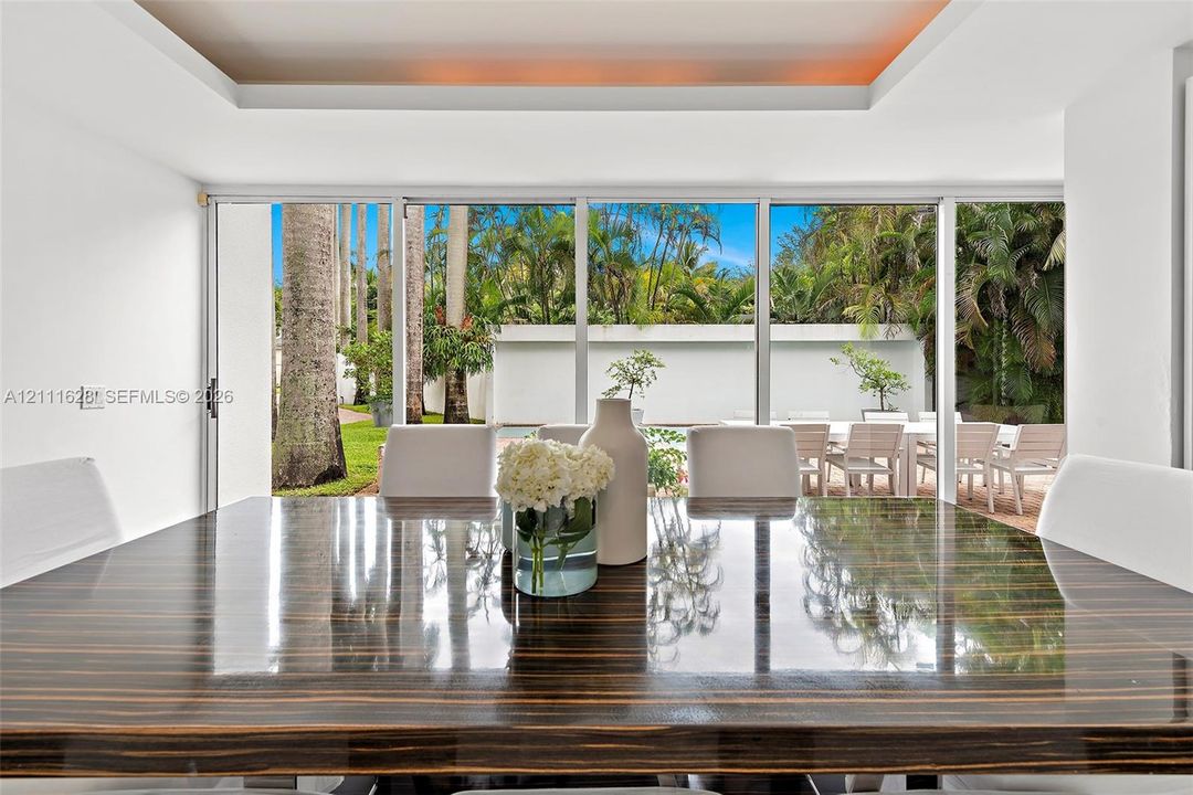 Floor-to-ceiling glass sliding doors, recessed tray ceiling with accent lighting, and expansive wall of windows overlooking a private outdoor space